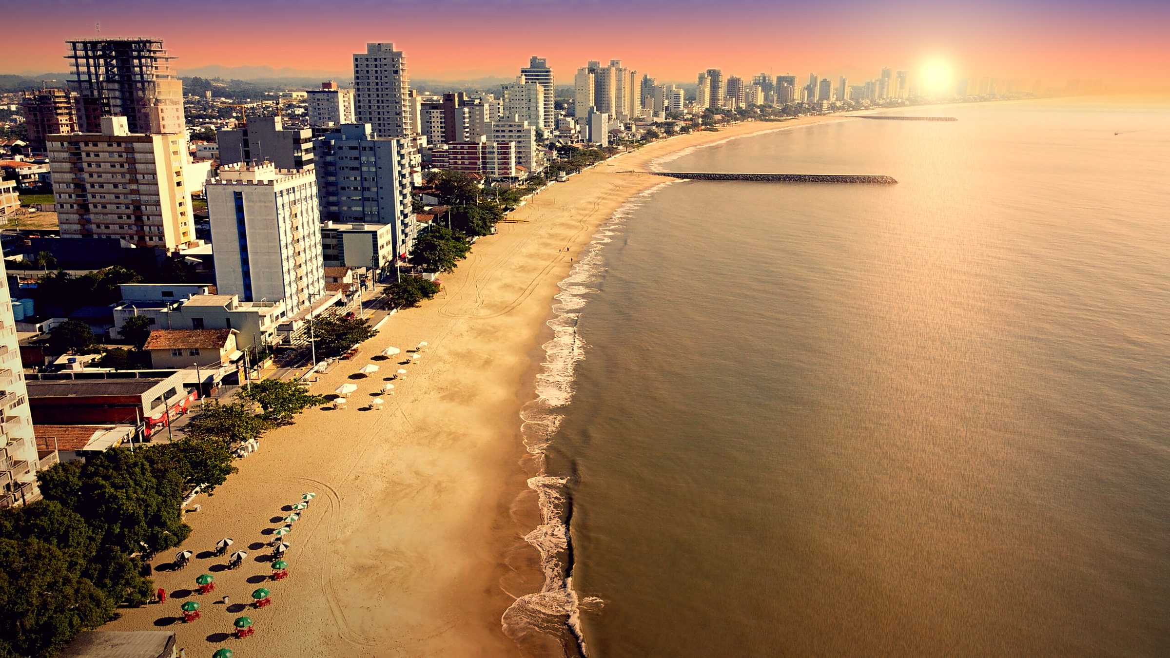 Vista aérea da praia de Balneário Piçarras ao pôr do sol, com prédios na orla
